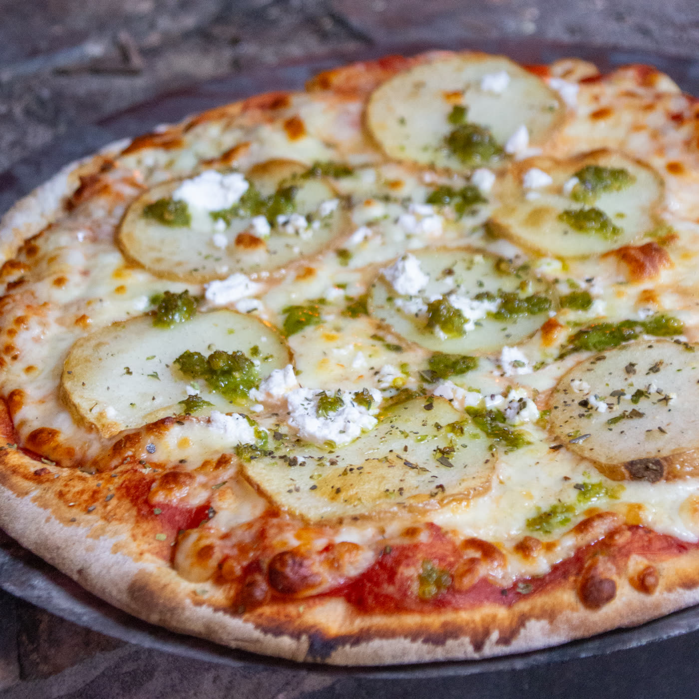 A woodfired potato pizza with feta and basil pesto, fresh from the oven floor